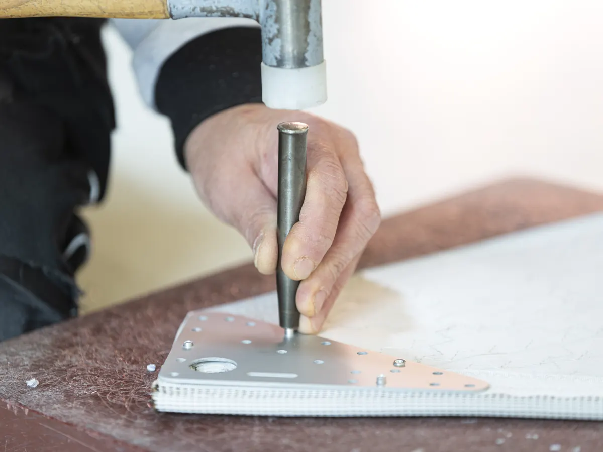 Handwerk aan een zeil met hamer en pons